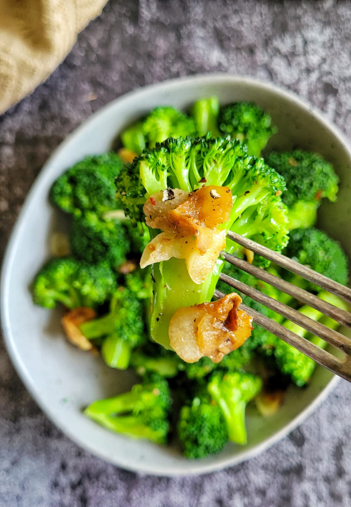 fork piercing pieces of crispy garlic and a broccoli floret over a bowl with the rest