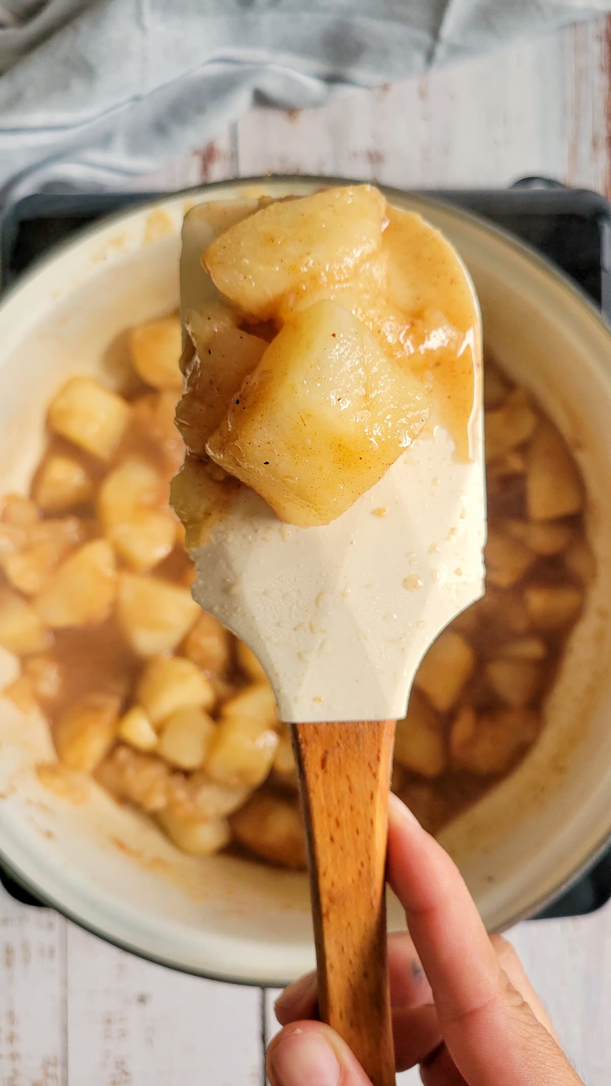 hand with a spatula holding up some cooked pear chunks over a pot of the rest of them