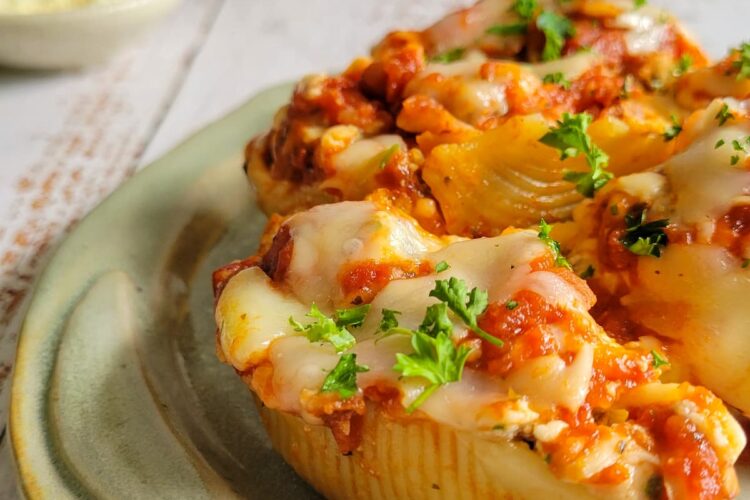3 stuffed pasta shells on a plate with cheese and chopped parsley
