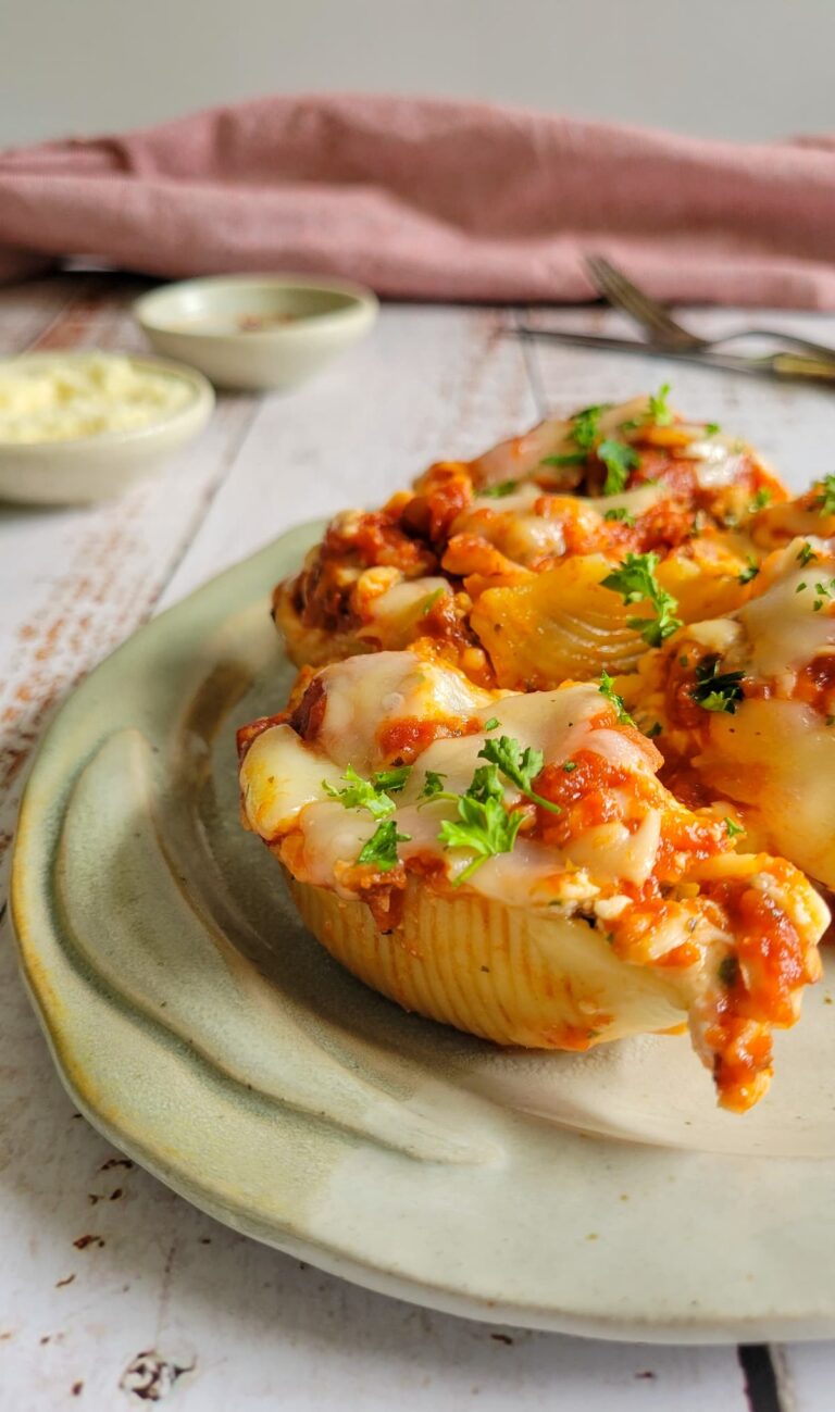3 stuffed pasta shells on a plate with cheese and chopped parsley