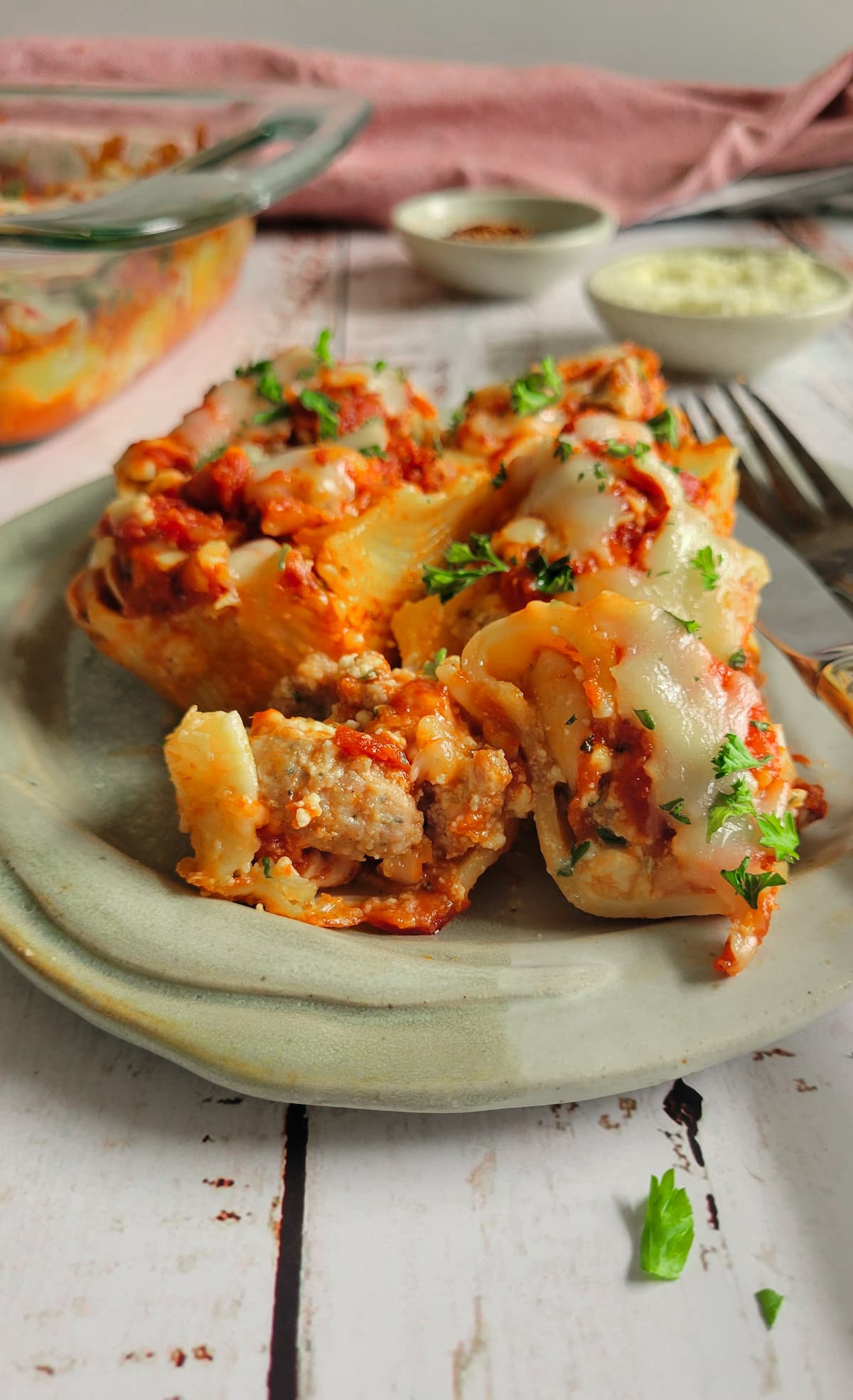 stuffed pasta shells on a plate with cheese, tomato sauce and fresh chopped parsley, the one in the front is cut in half