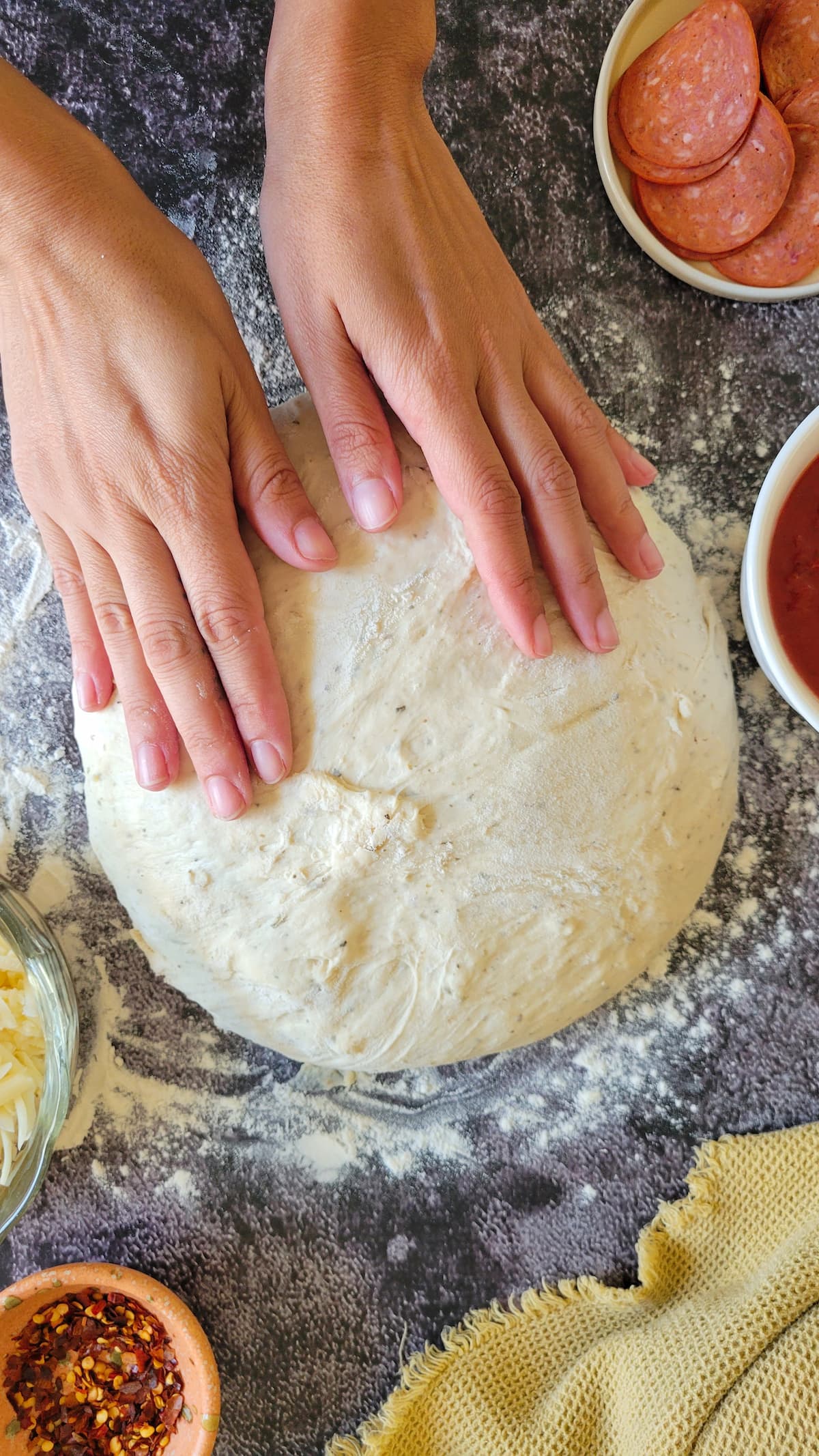 hands on a ball of dough, bowls of pizza toppings surrounding it