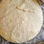 ball of pizza dough on a floured surface, mozzarella and tomato sauce in the background