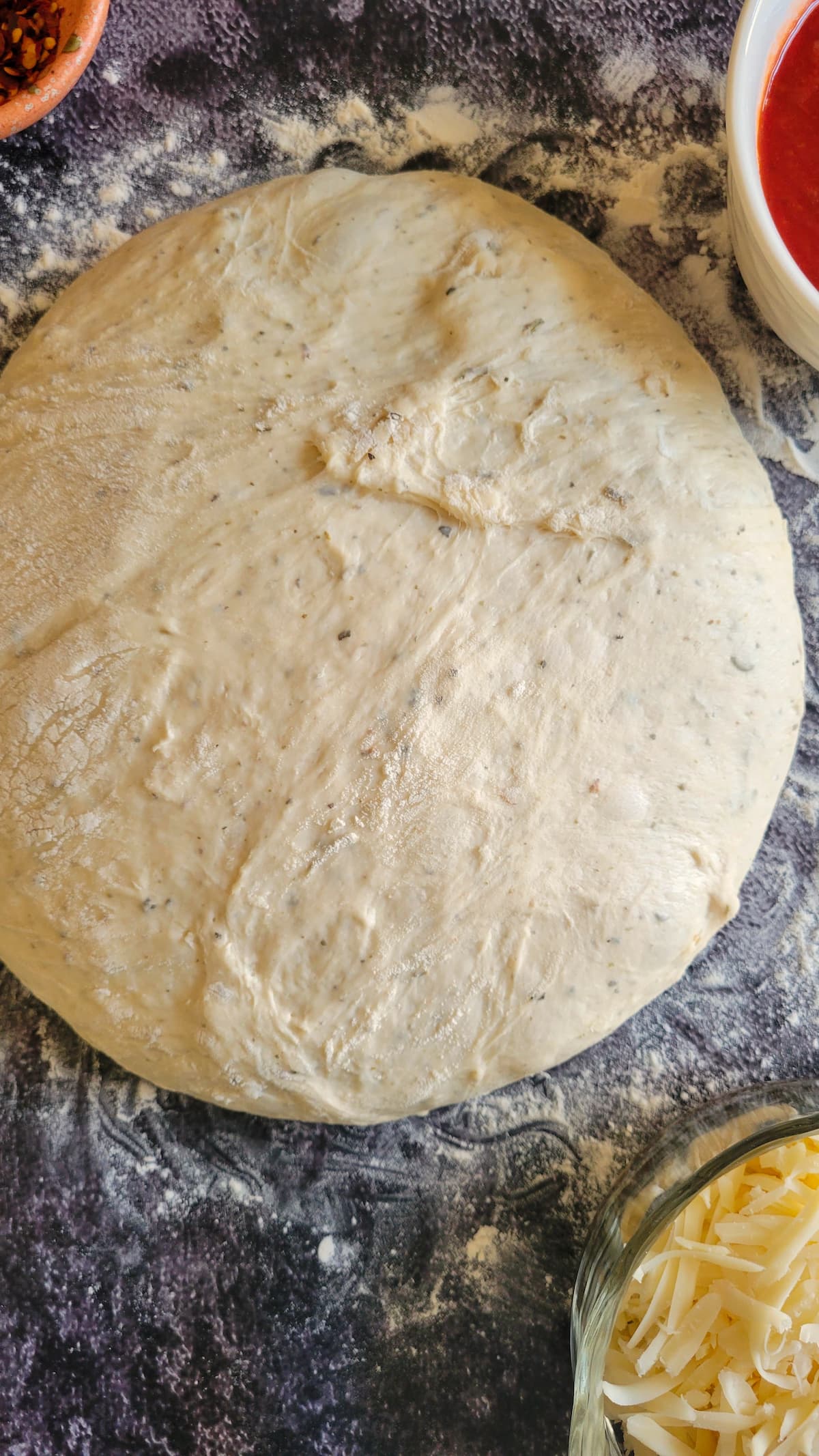 ball of pizza dough on a floured surface, mozzarella and tomato sauce in the background