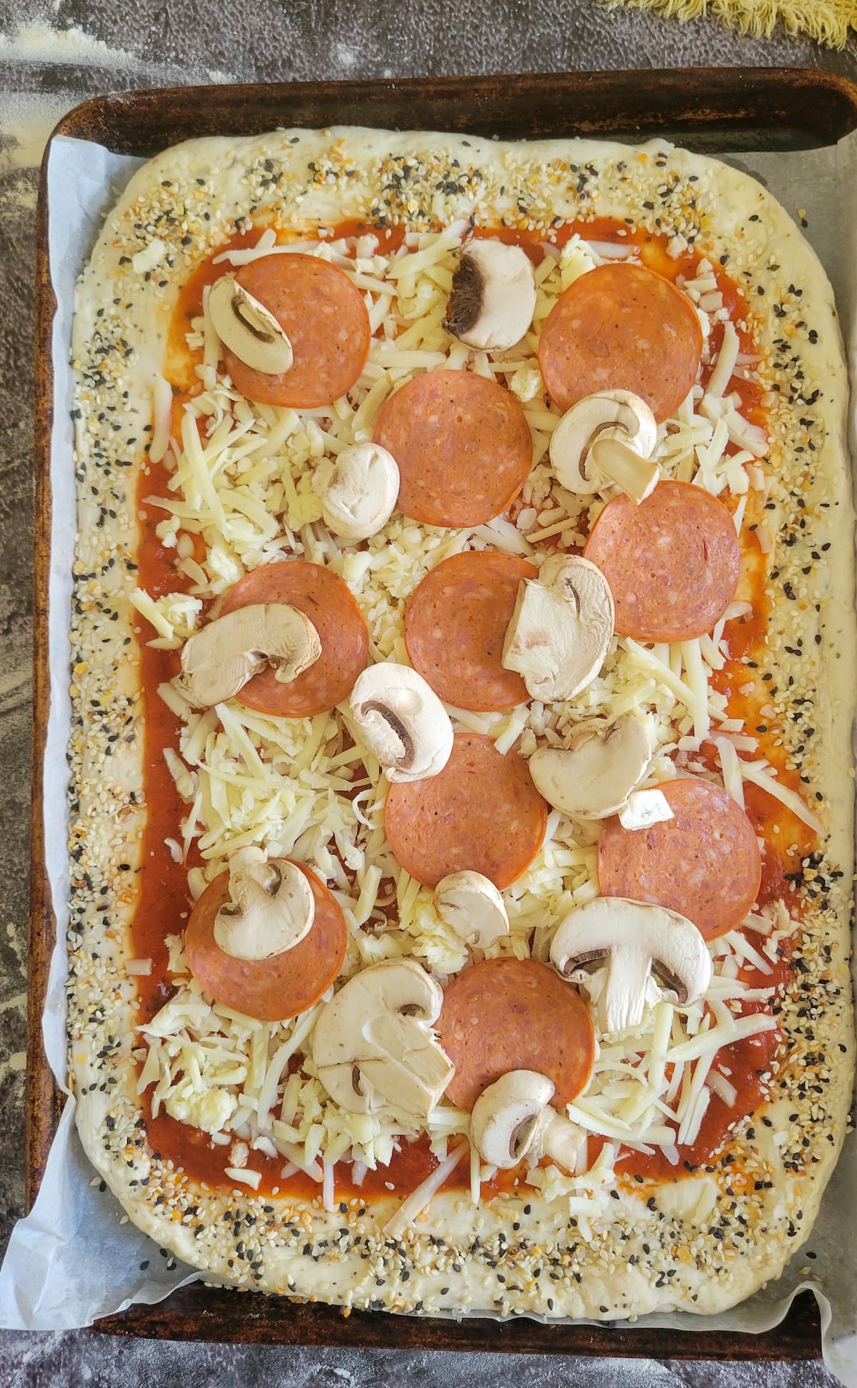 pizza topped with tomato sauce, mozzarella, mushrooms and pepperoni on a parchment lined baking sheet