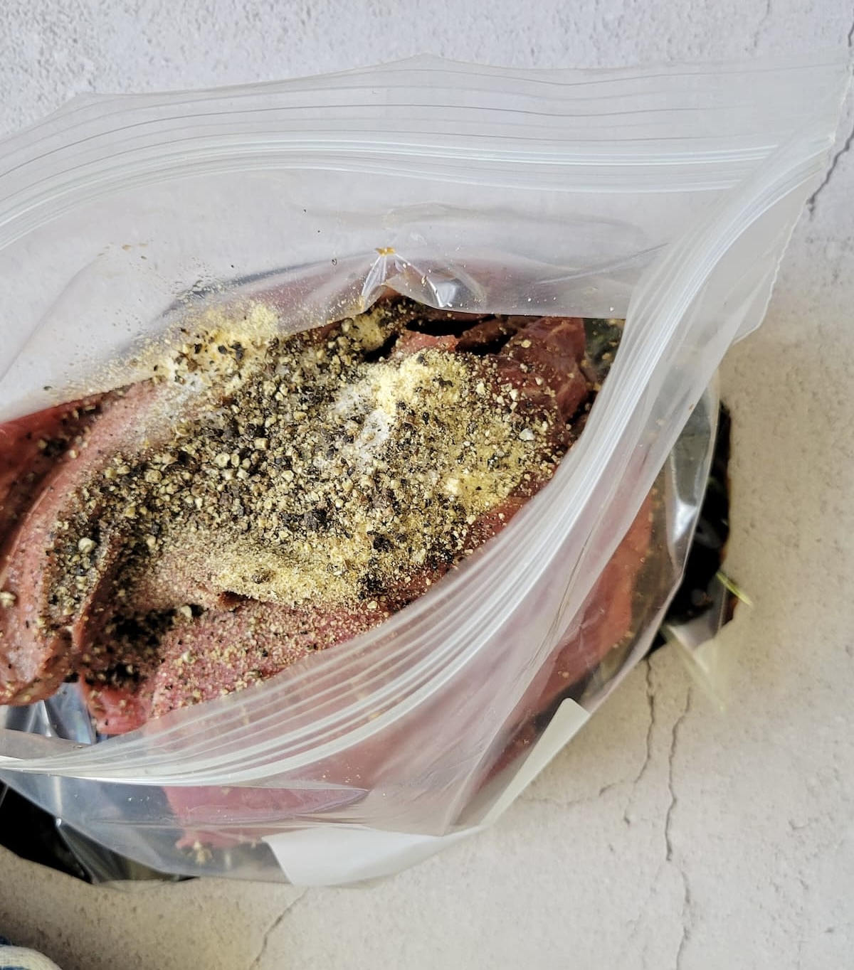 fresh cracked pepper and other spices and soy sauce with sliced raw meat in an opened ziploc bag