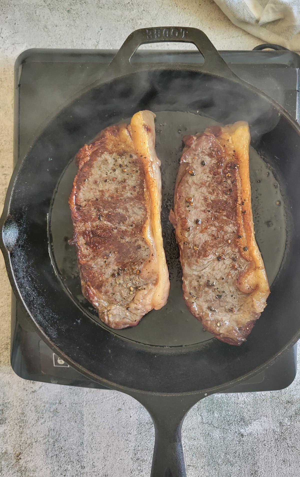 two steaks searing in a cast iron skillet