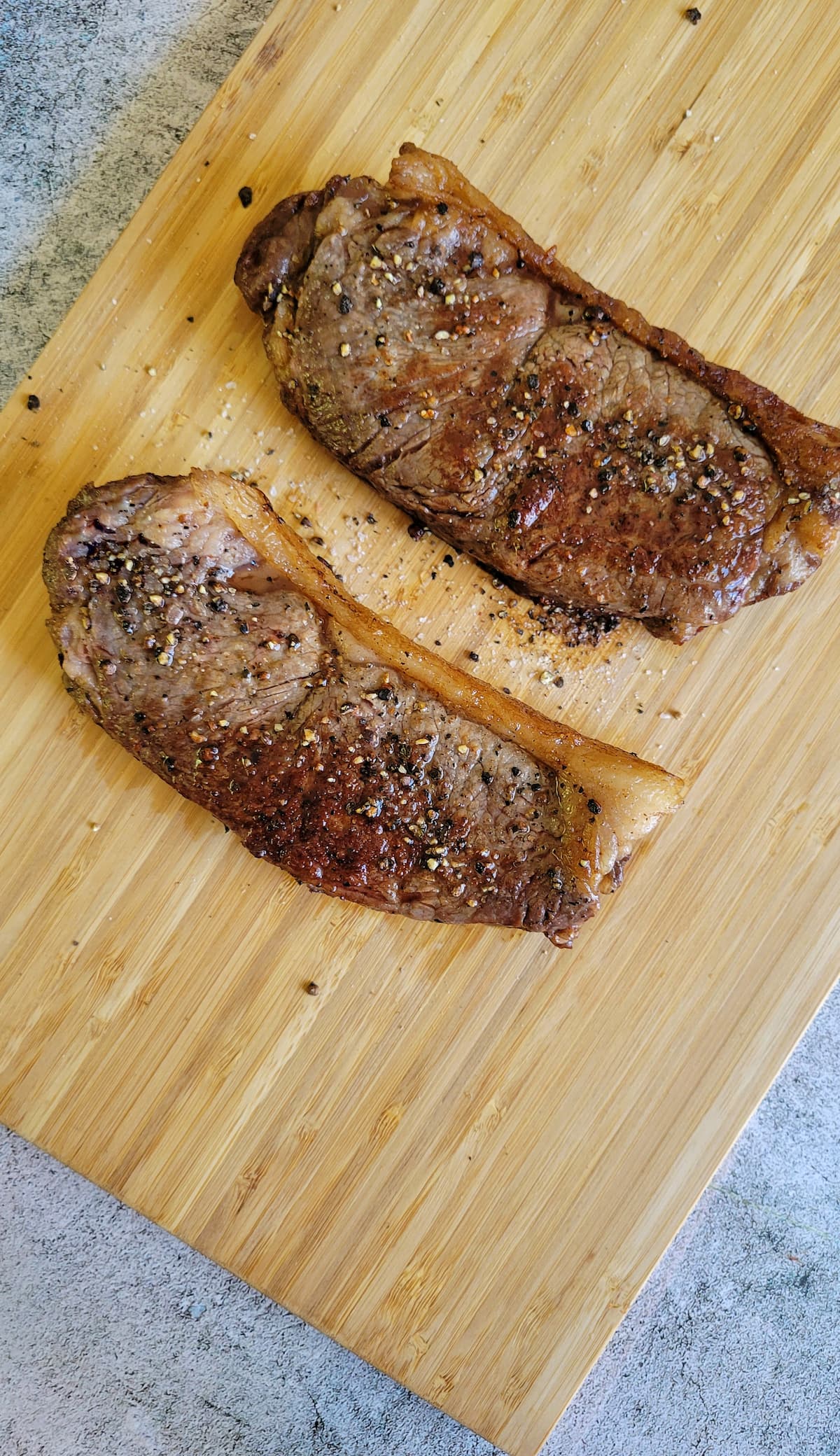 two seared salt and pepper seasoned steaks on a cutting board