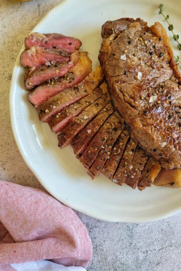 two steaks on a plate, one sliced and pink, other whole