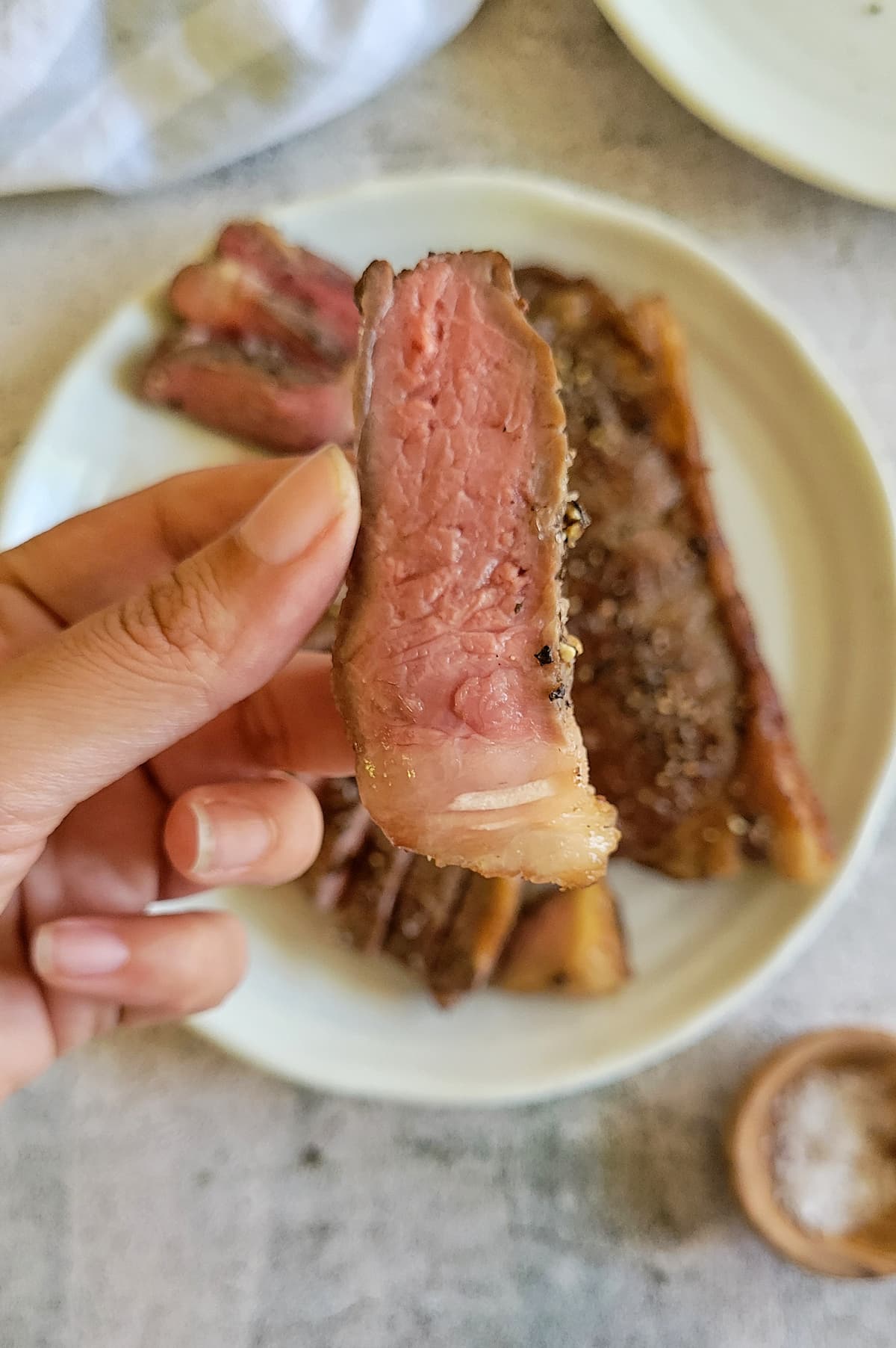 hand holding up a piece of medium rare cooked steak over a plate of the rest