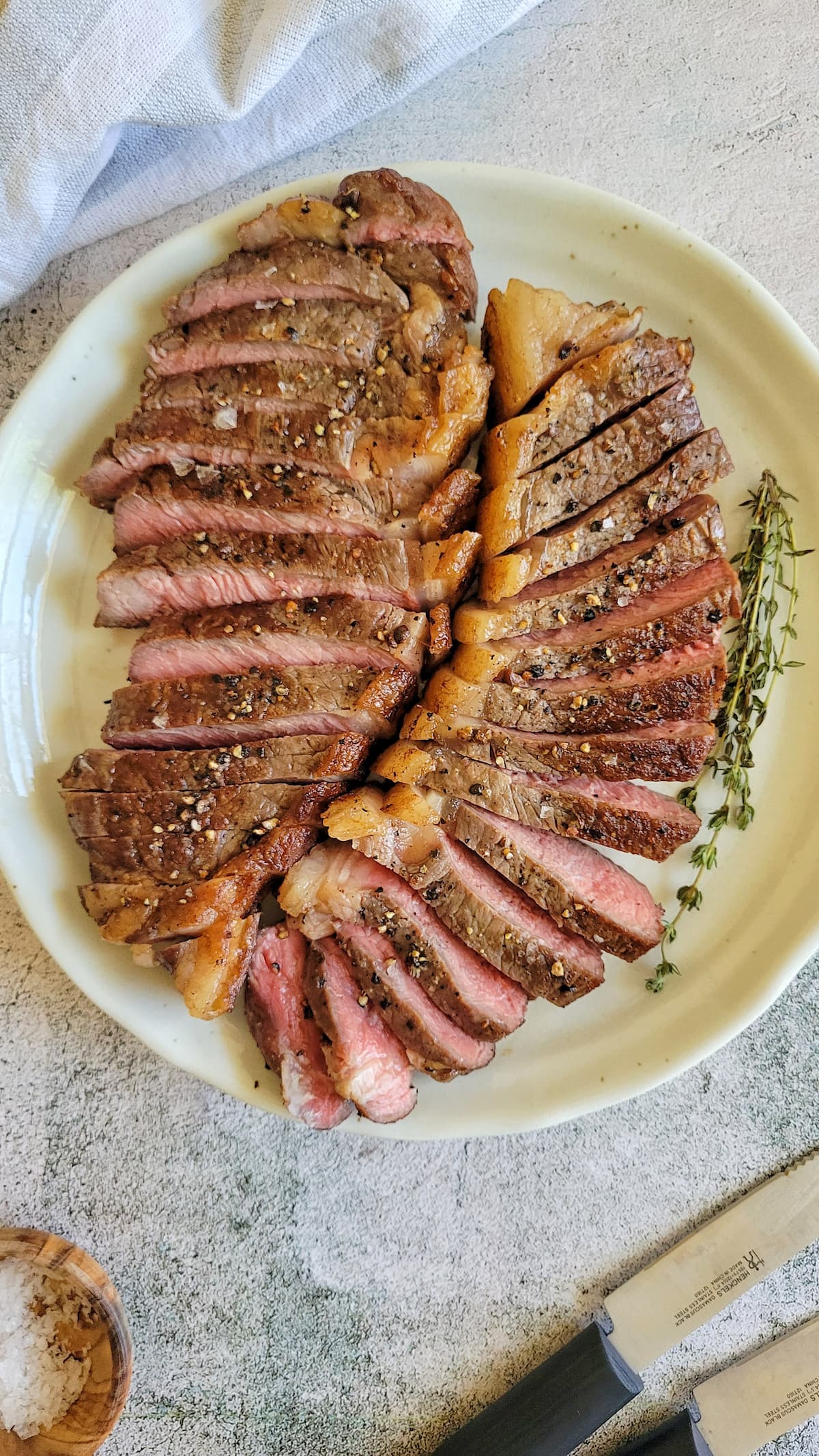 two sliced rare salt and pepper seasoned steaks on a plate with herbs
