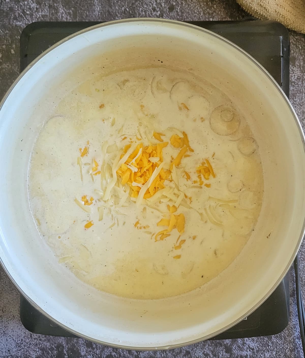 shredded mozzarella and cheddar cheese in a pot with cream and shallots