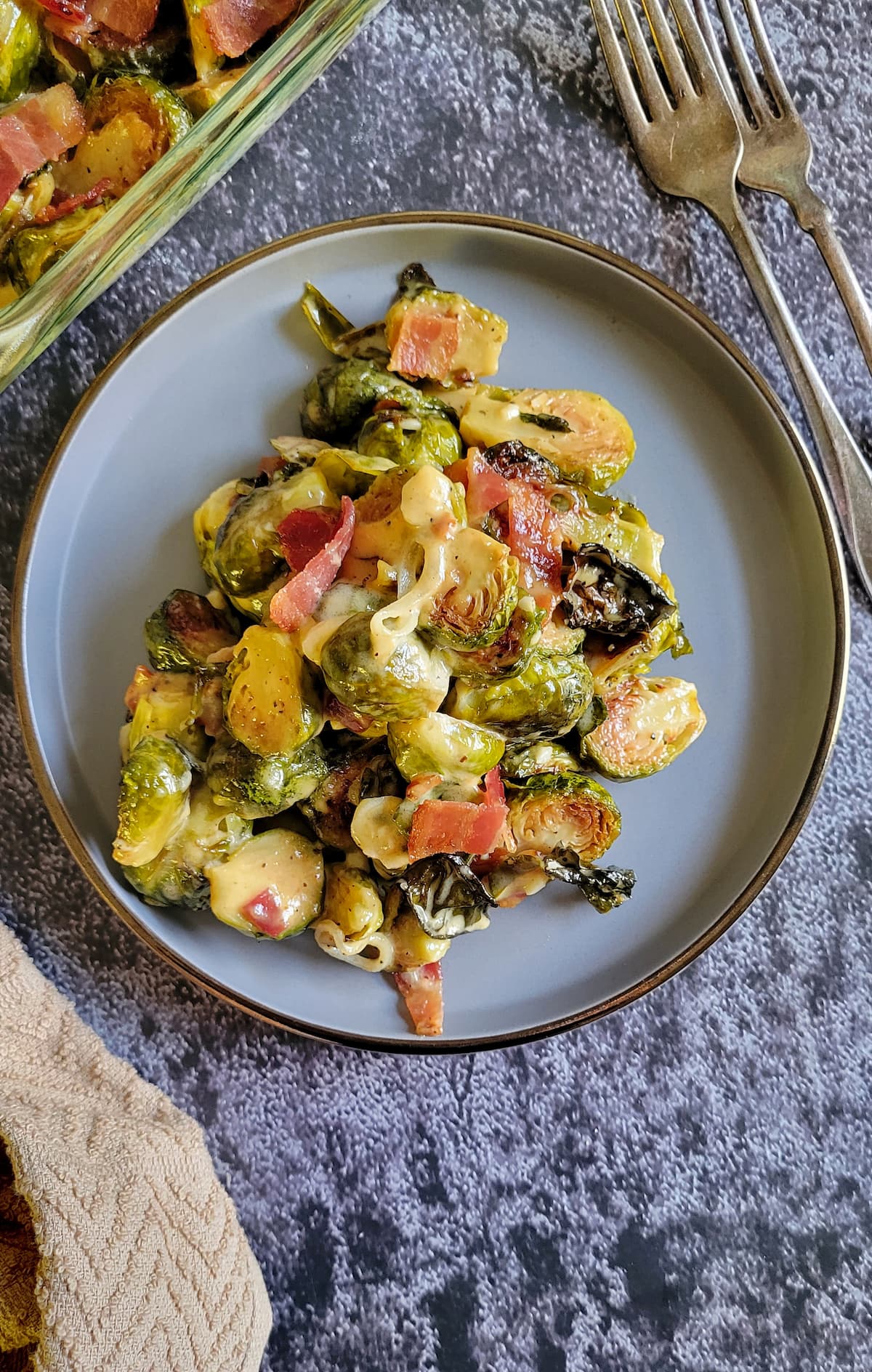 plate with brussels sprouts and bacon, dish with more in the background next to two forks
