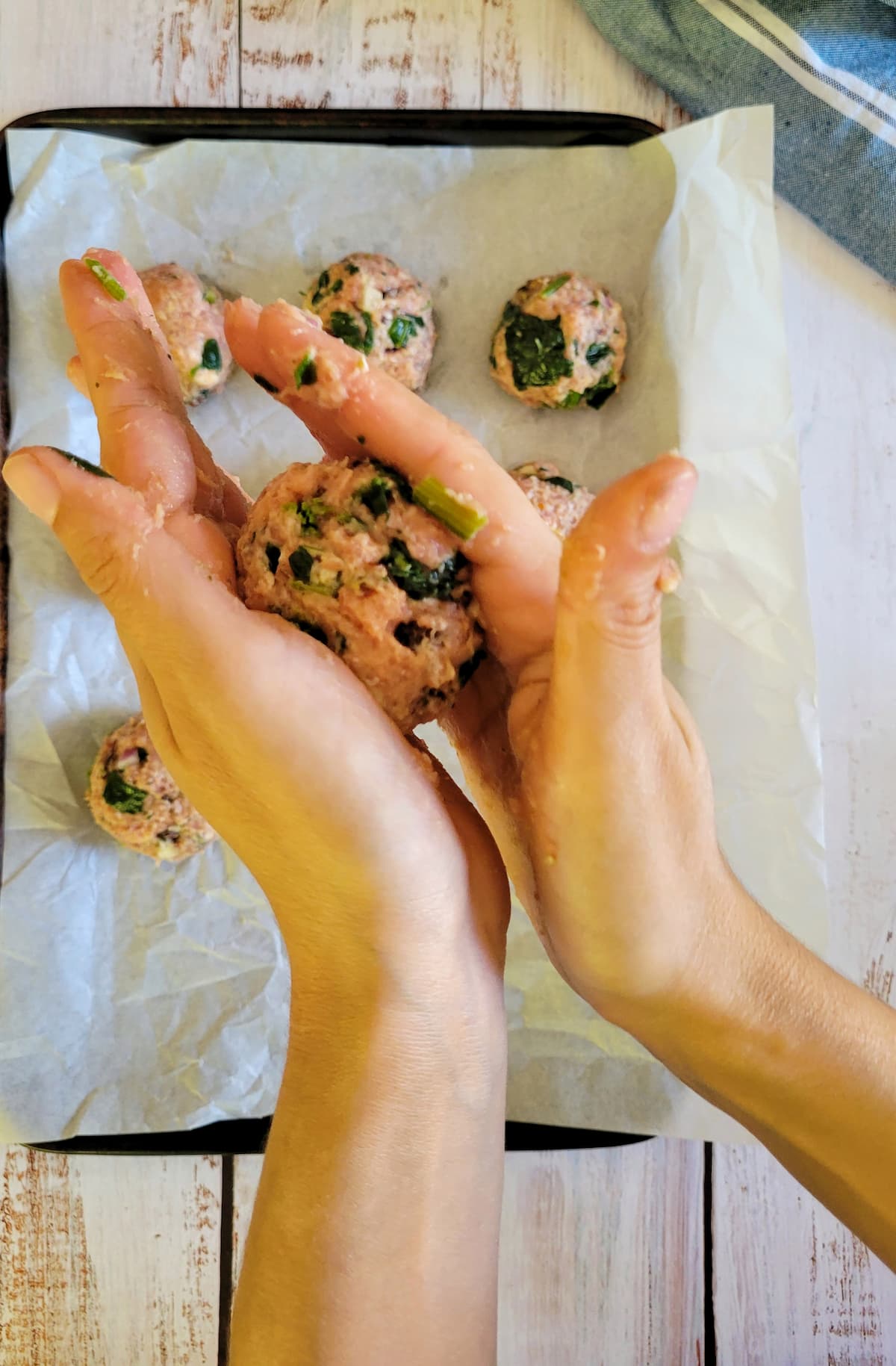 hands rolling a meatball over a parchment lined baking sheet with the rest of them
