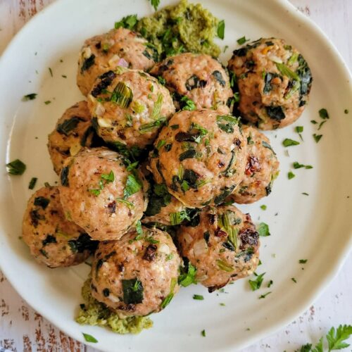turkey spinach meatballs stacked on a plate with pesto and chopped fresh parsley, lemon in the background