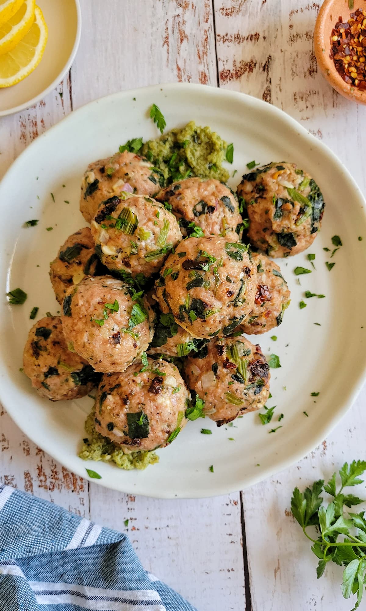turkey spinach meatballs stacked on a plate with pesto and chopped fresh parsley, lemon in the background