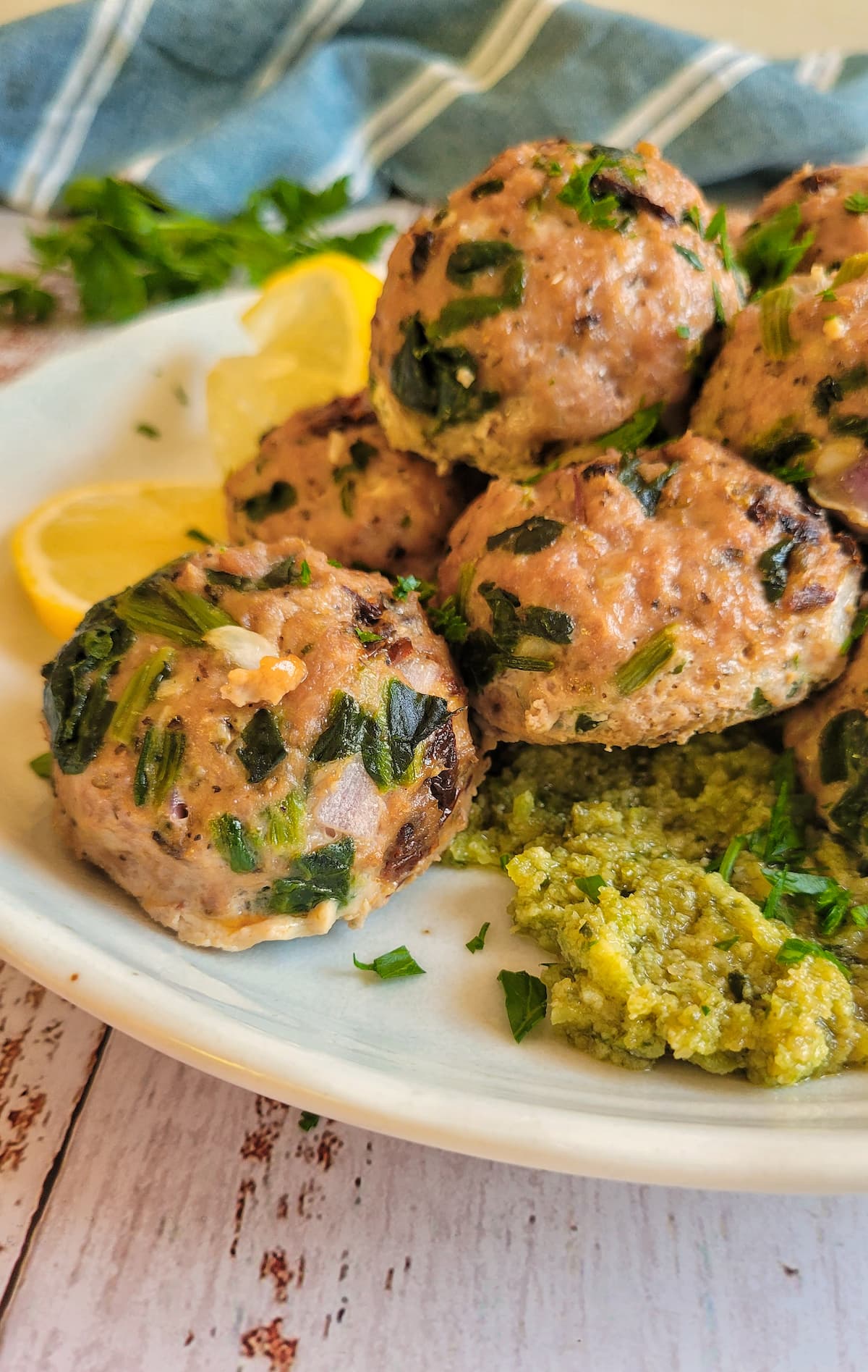 turkey spinach meatballs stacked on a plate with pesto and lemon