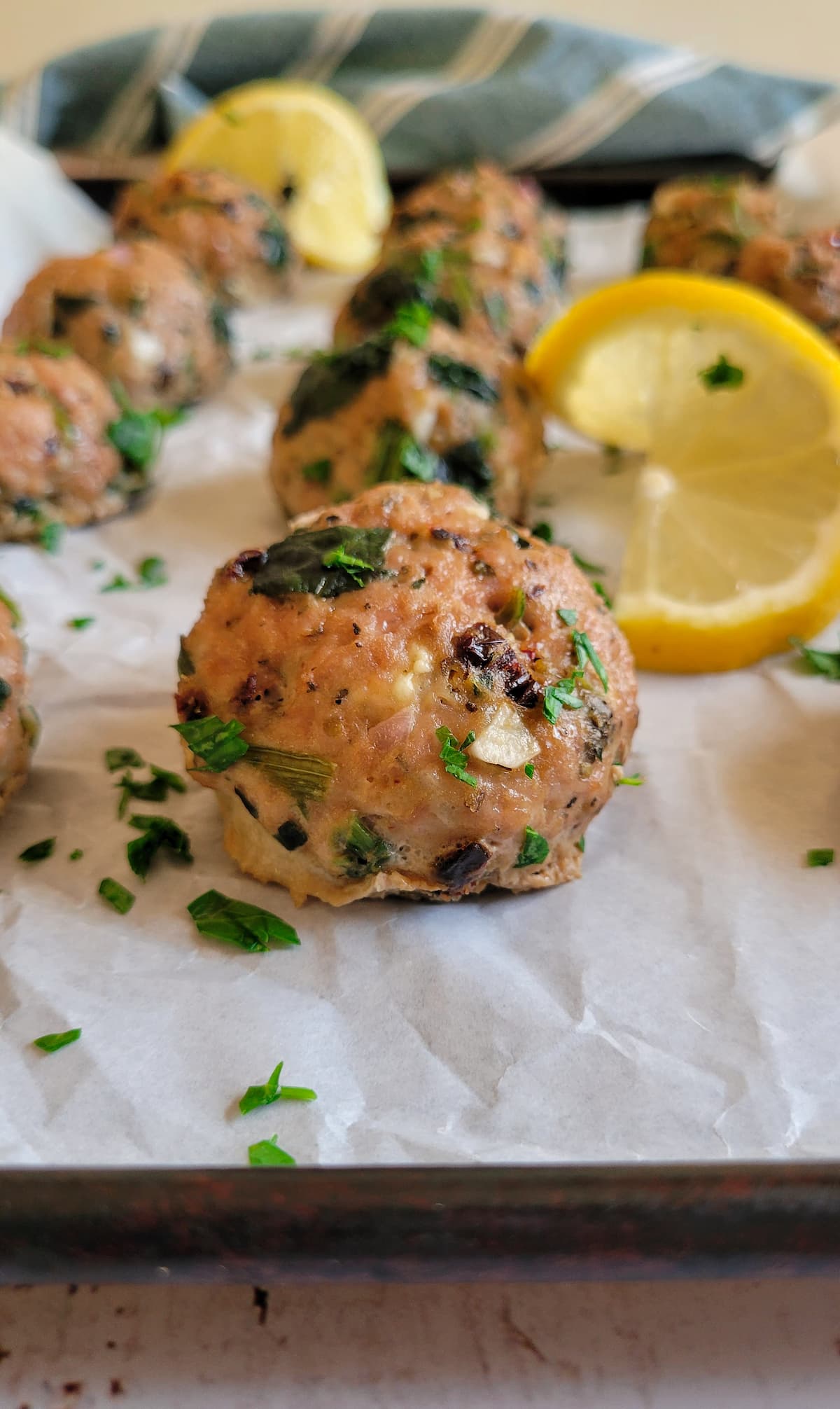 close up of a meatball on a parchment lined baking sheet with lemon and more meatballs in the background