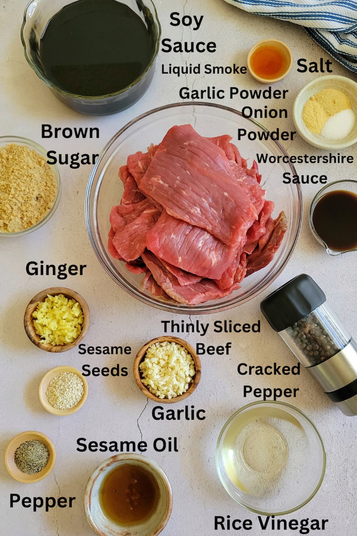 ingredients for recipe for beef jerky in a dehydrator - thinly sliced beef, soy sauce, liquid smoke, salt, onion powder, garlic powder, worcestershire sauce, brown sugar, pepper, cracked pepper, sesame seeds, sesame oil, ginger, garlic, rice vinegar