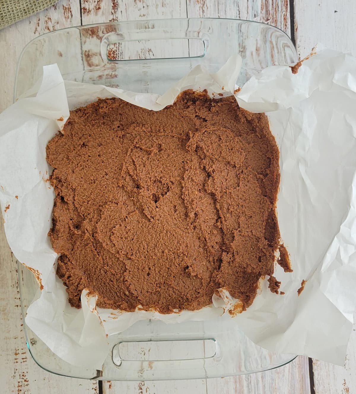 brownie batter spread out into a glass baking dish lined with parchment