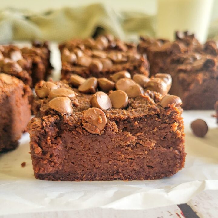 close up of a brownie topped with chocolate chips, more brownies in the background with a glass of milk