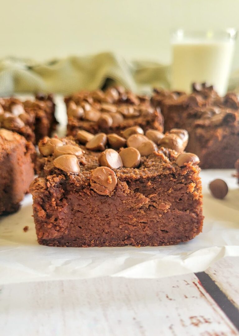 close up of a brownie topped with chocolate chips, more brownies in the background with a glass of milk