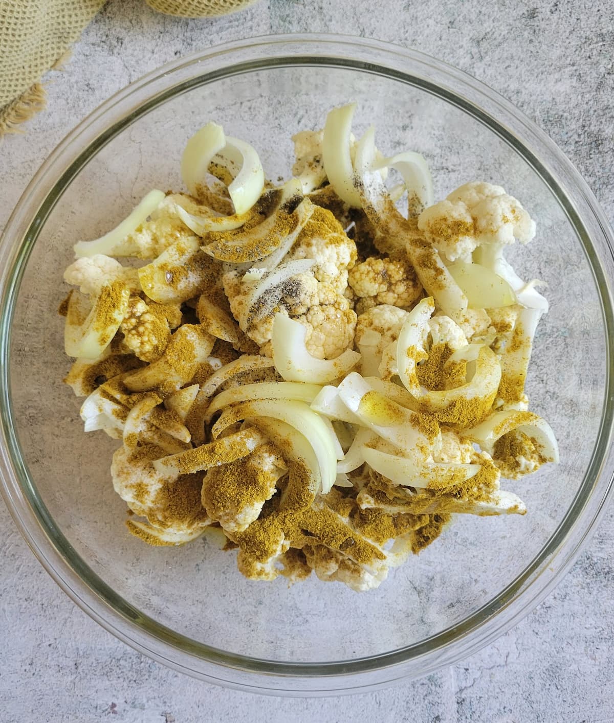 bowl of raw cauliflower florets, sliced white onions and seasonings unmixed