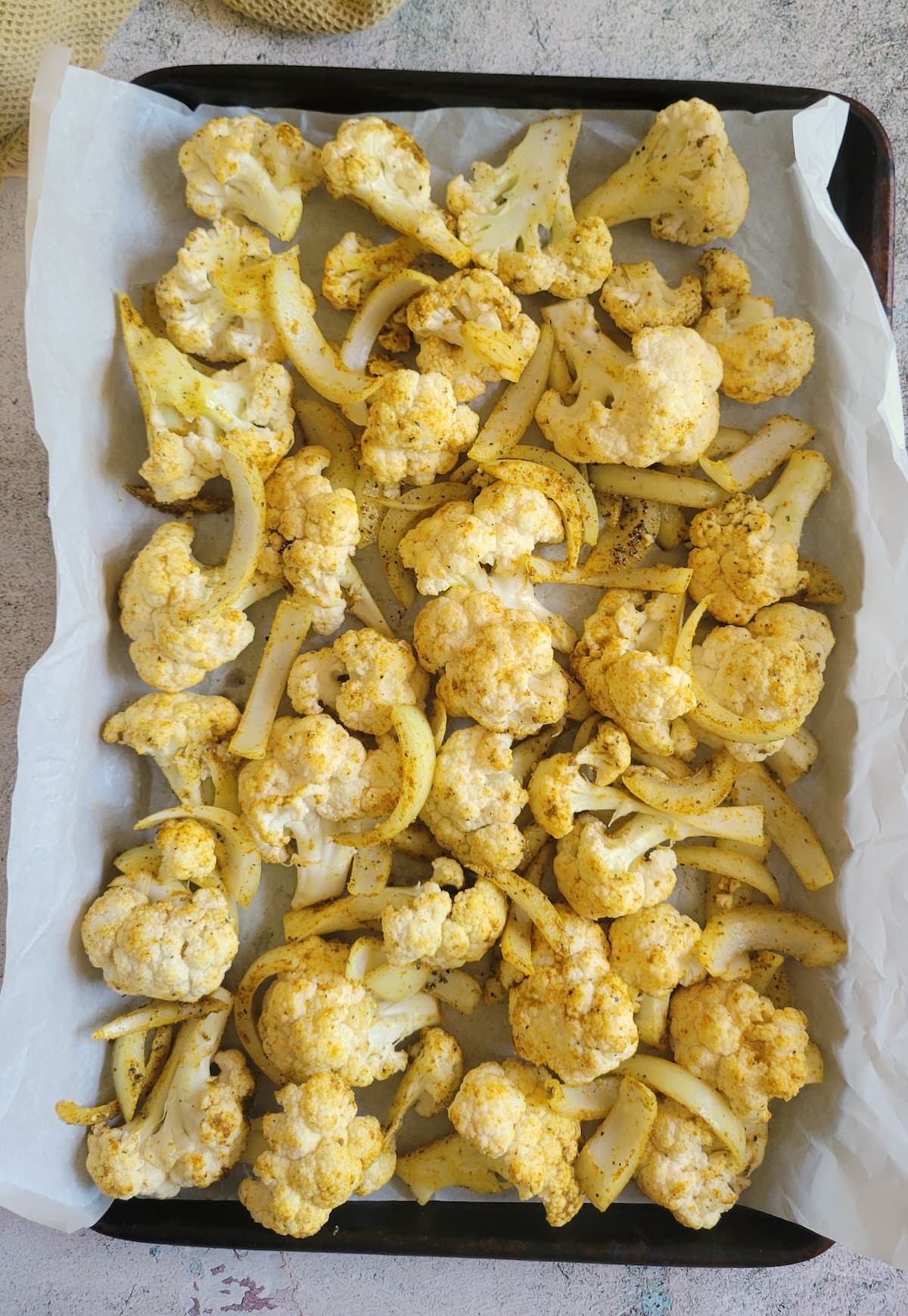raw seasoned cauliflower florets and sliced white onions on a parchment lined baking sheet