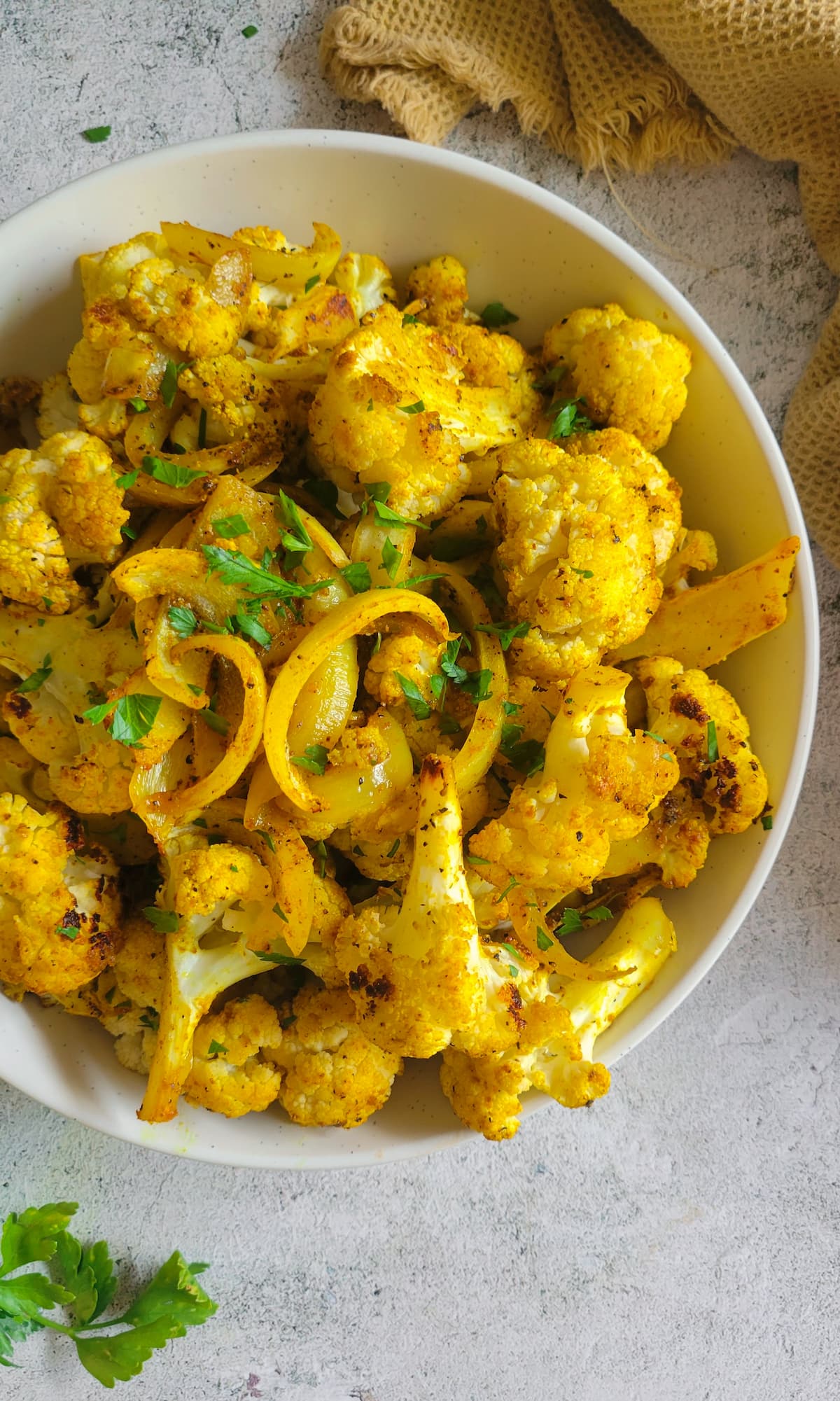 bowl of curried cauliflower with sliced white onions and chopped fresh parsley