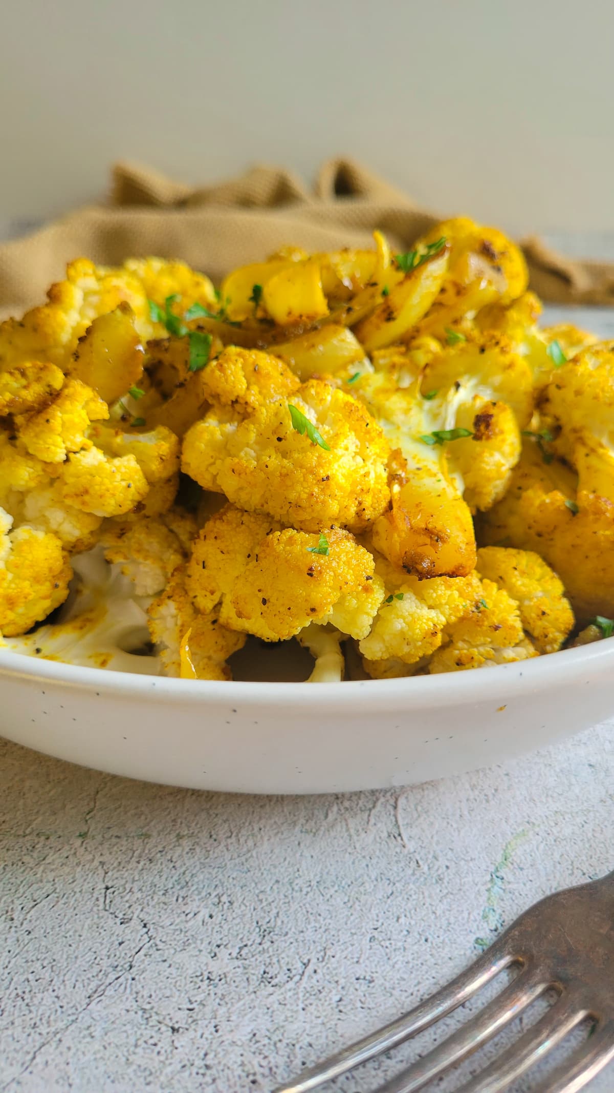 side view of a bowl of yellow cauliflower with chopped fresh parsley, fork in the front