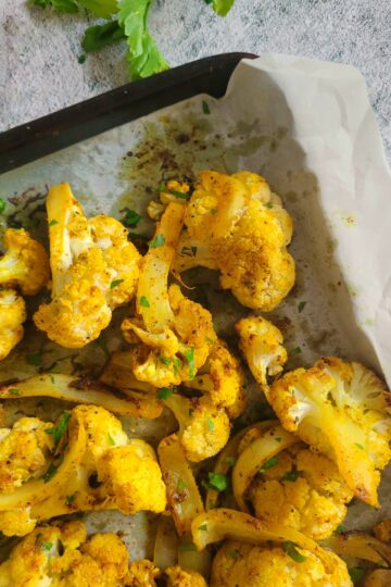 roasted yellow cauliflower on a parchment lined baking sheet with sliced white onions and chopped fresh parsley