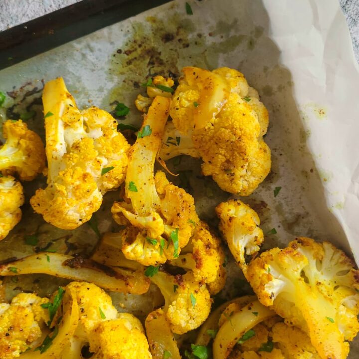 roasted yellow cauliflower on a parchment lined baking sheet with sliced white onions and chopped fresh parsley