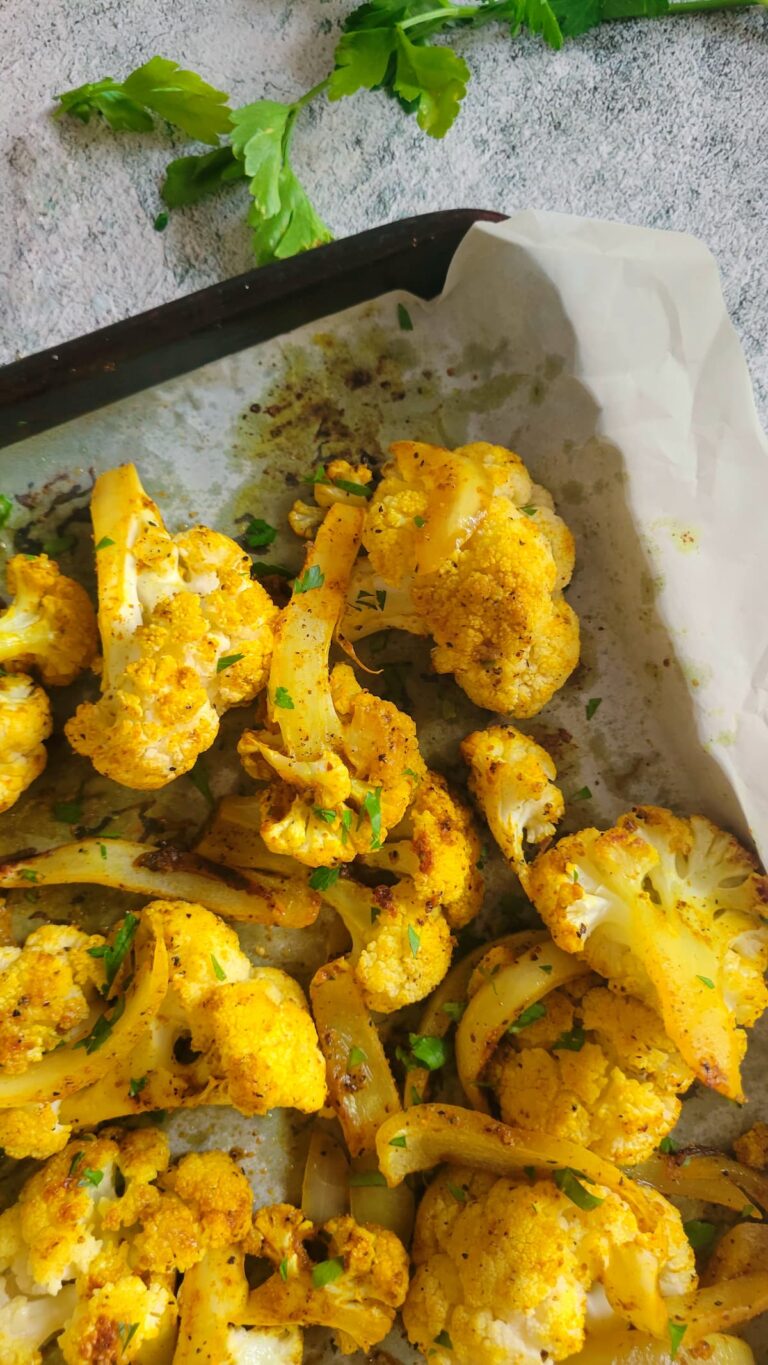 roasted yellow cauliflower on a parchment lined baking sheet with sliced white onions and chopped fresh parsley