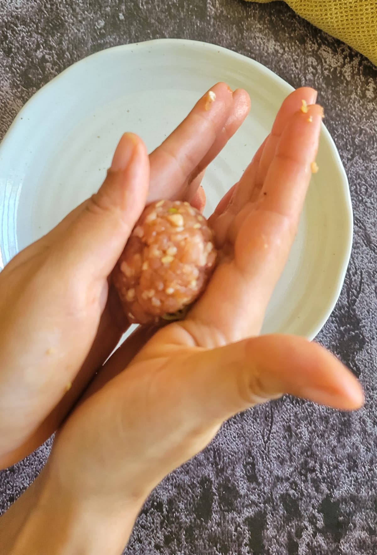 hand rolling a meatball over a plate