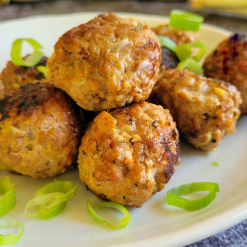 meatballs stacked on a plate garnished with green onions