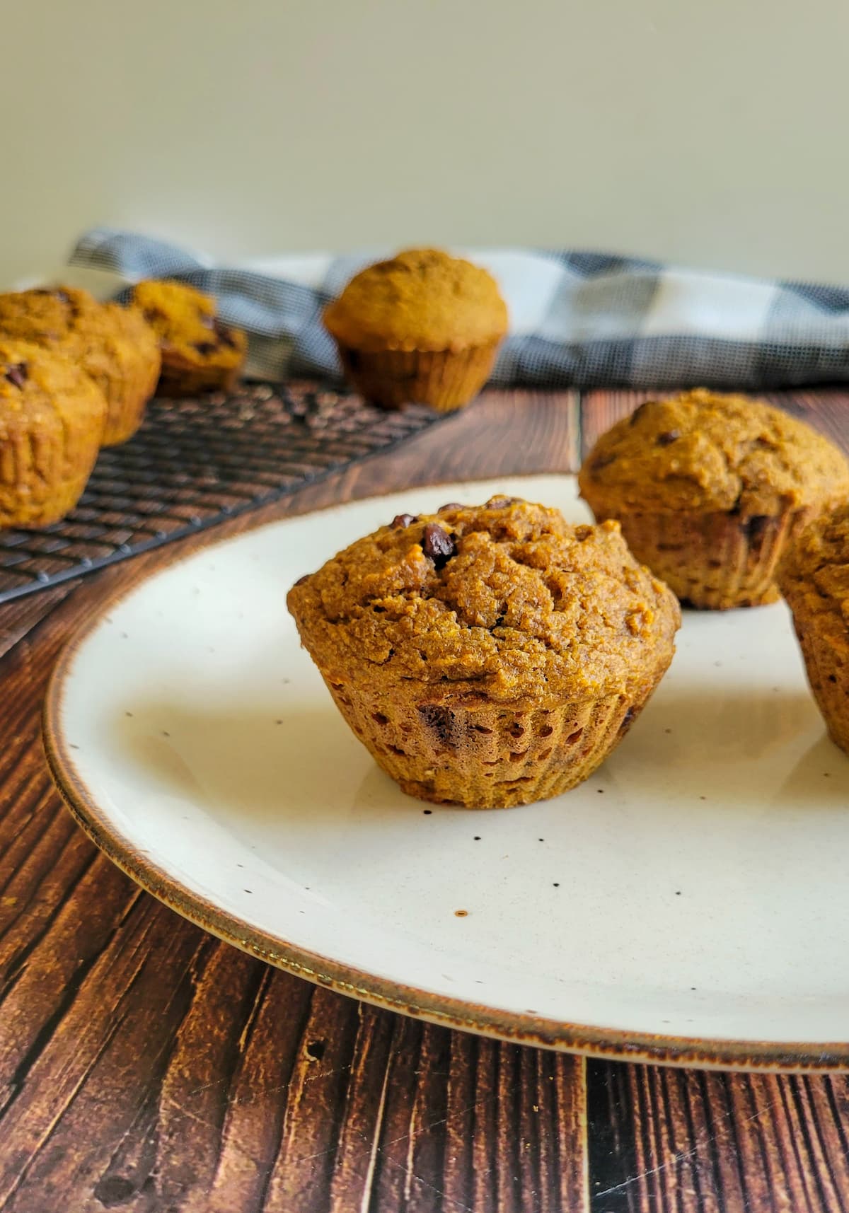 chocolate chip pumpkin muffins on a plate, more on a wire rack in the background