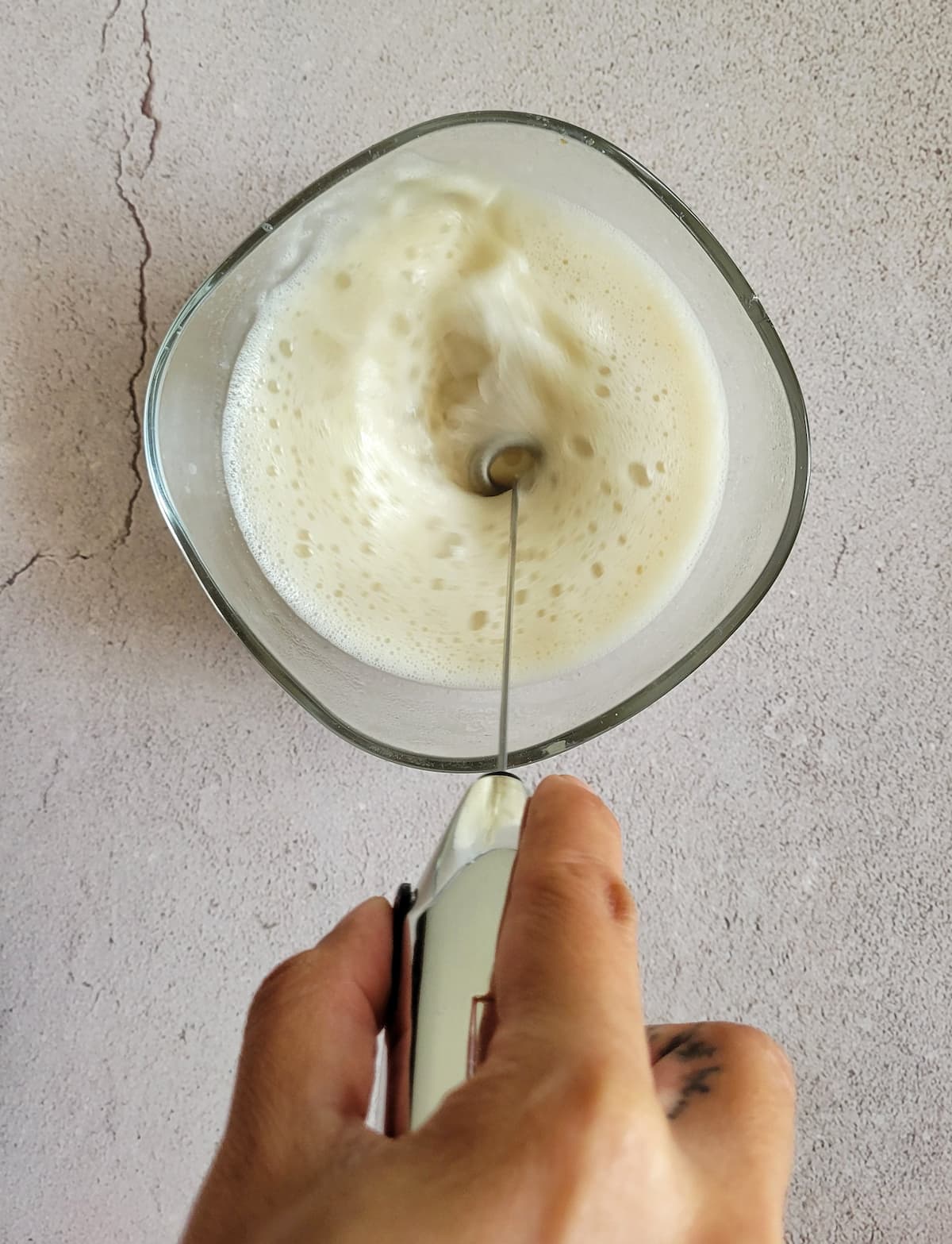 hand with a frother frothing milk in a bowl