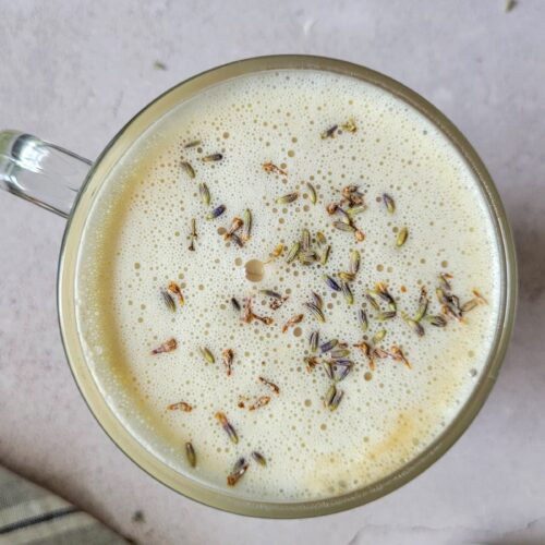 london fog in a mug topped with frothy milk and lavender, milk frother and tea bag in the background