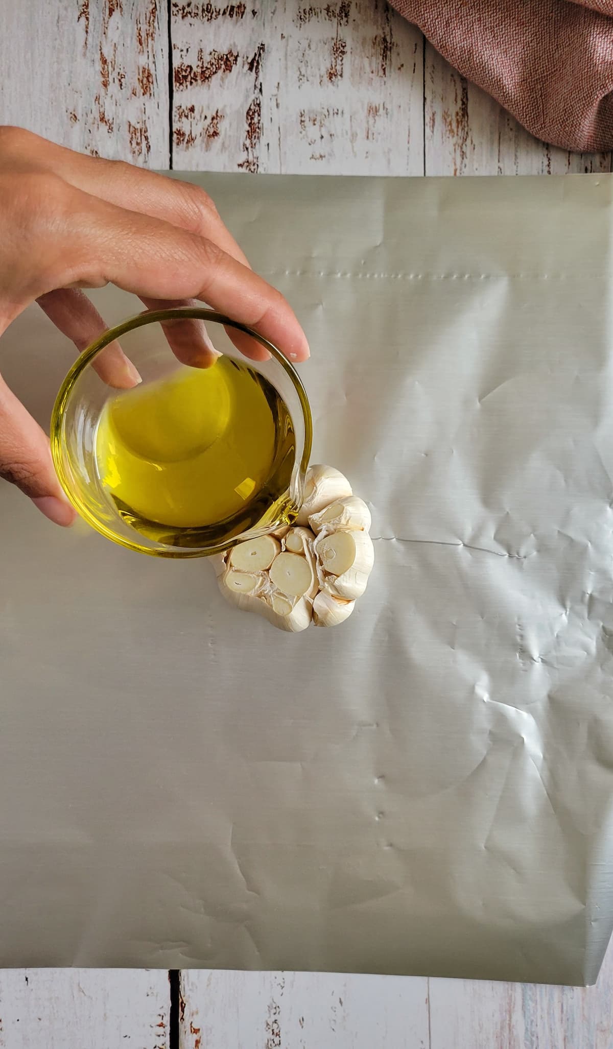 olive oil being drizzled onto a sliced raw garlic bulb in a piece of foil