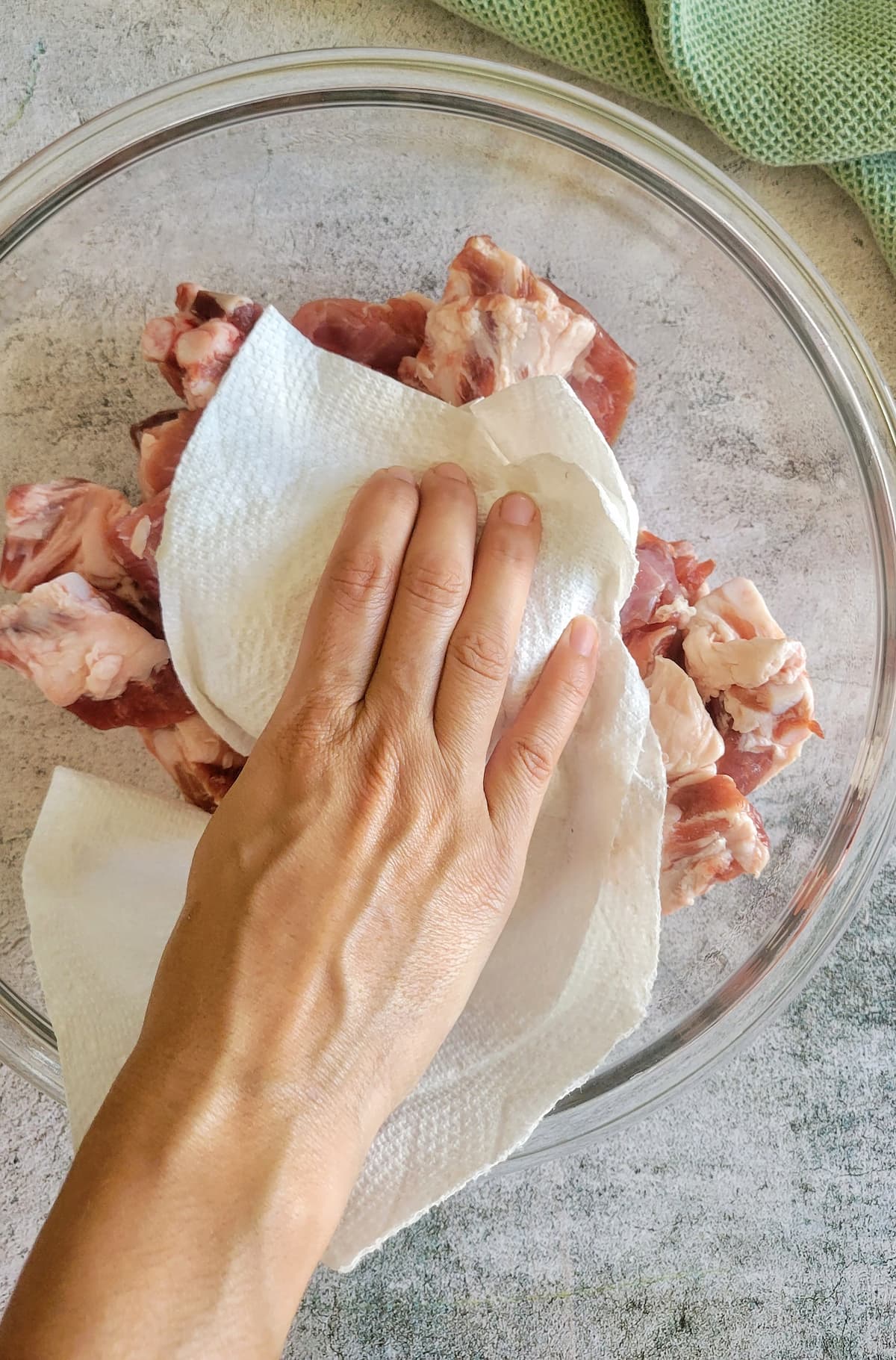 hand with a paper towel patting raw pork riblets down in a bowl