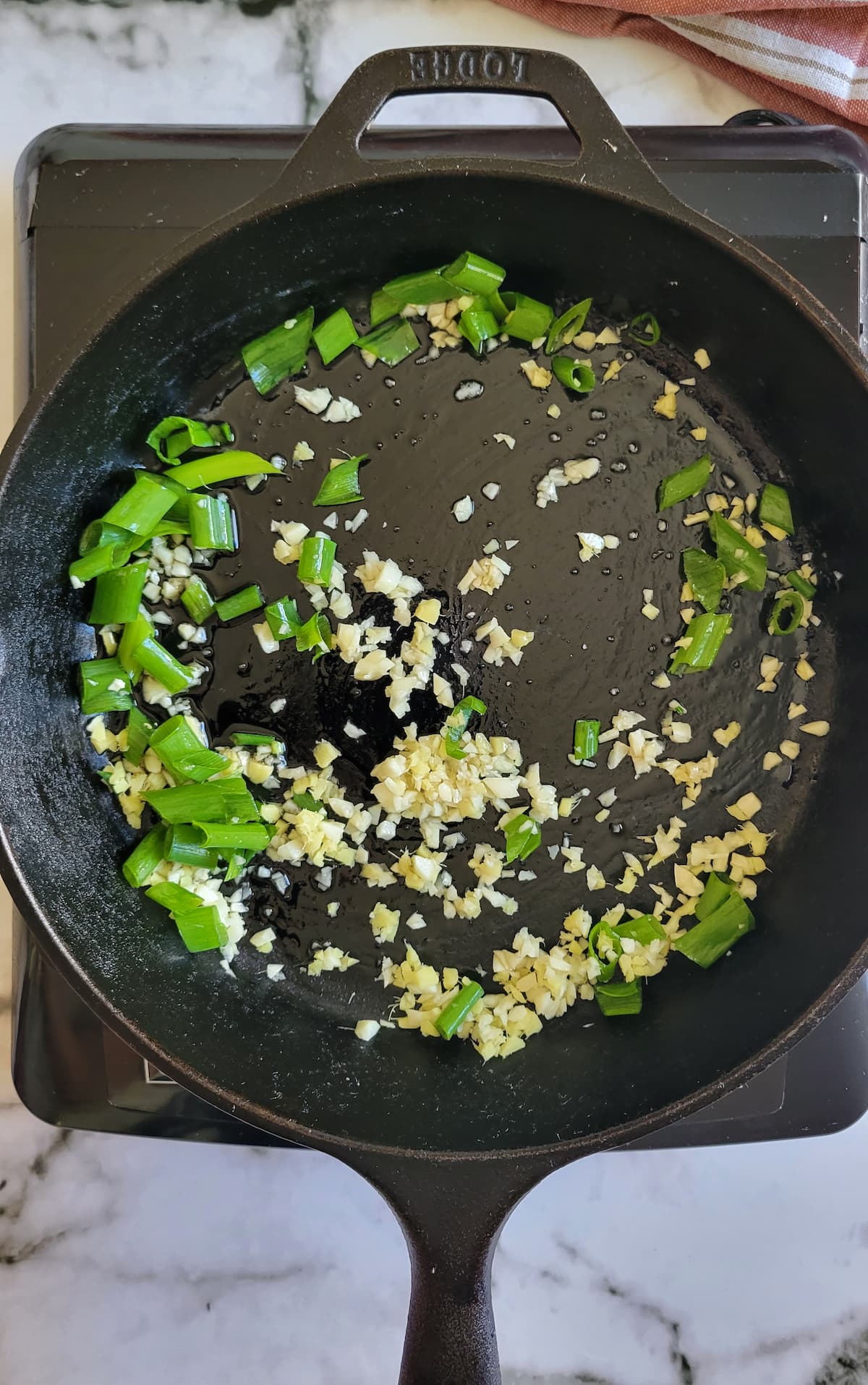 minced garlic, ginger and green onions cooking in a cast iron skillet on a burner