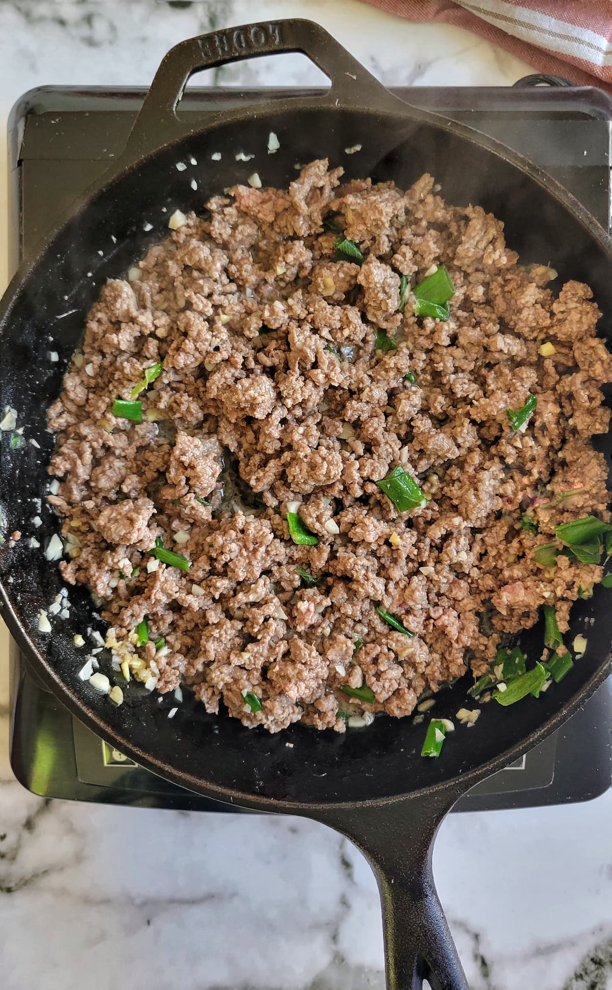 green onions, garlic and browned ground beef in a cast iron skillet on a burner