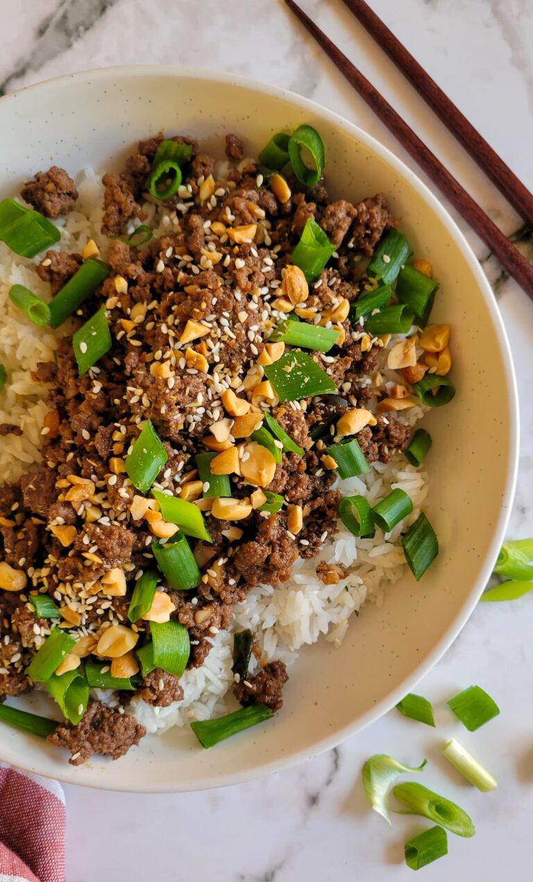 chopsticks next to a bowl with rice, ground beef, sesame seeds, chopped peanuts and green onions