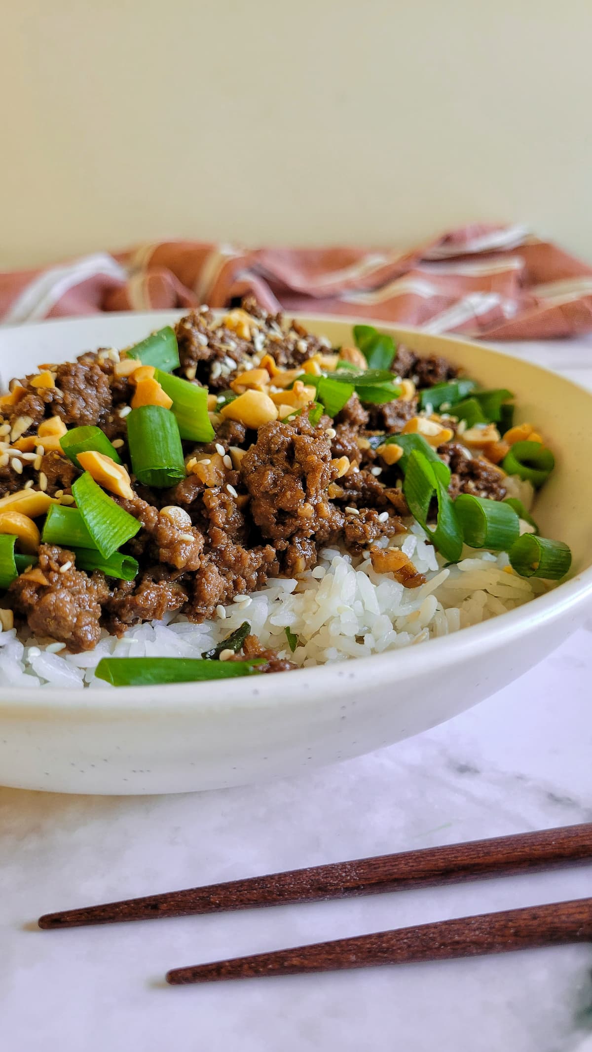 side view of ground beef with rice, peanuts, green onions and sesame seeds, chopsticks in the front
