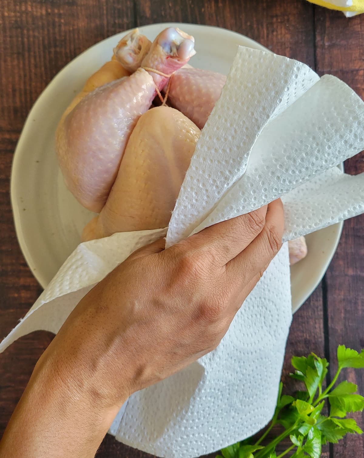 hand with a paper towel patting a whole raw chicken dry