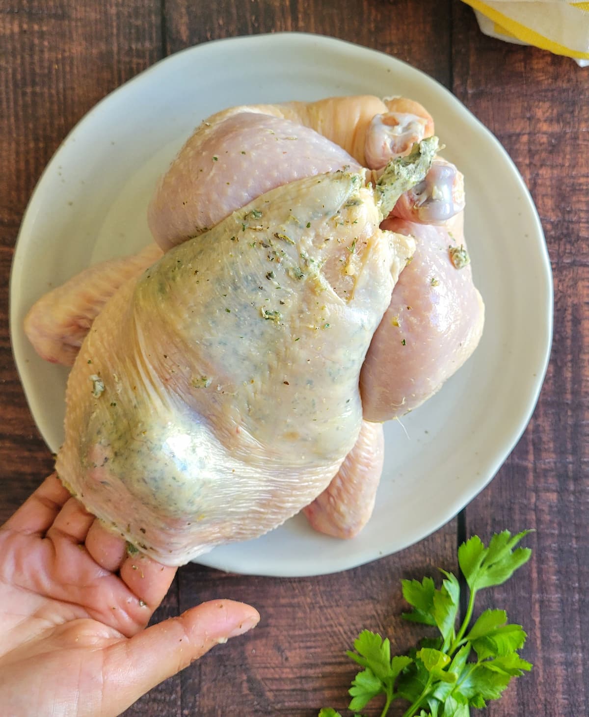 hands adding garlic butter underneath chicken skin on a raw whole chicken