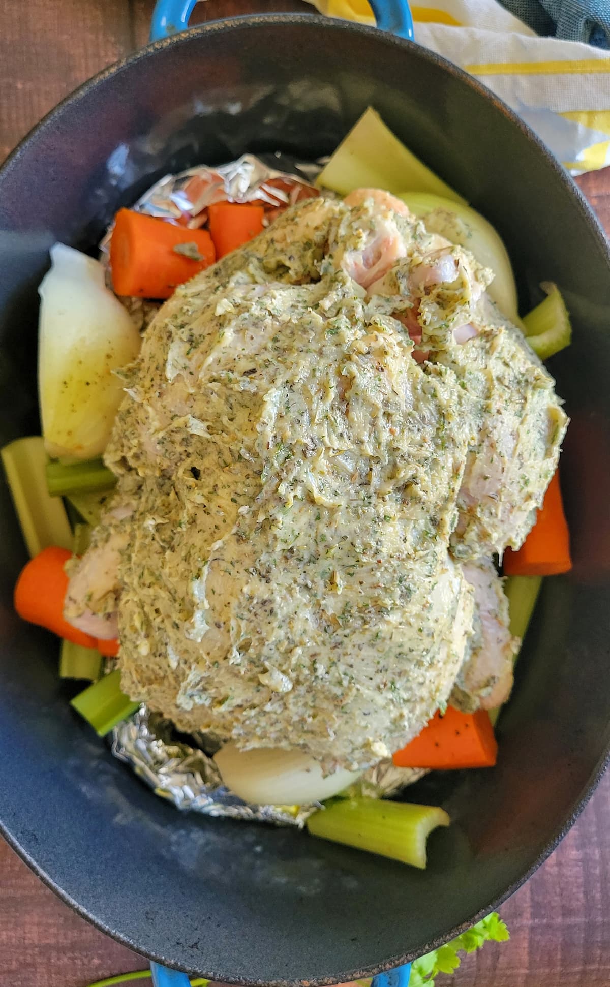 raw herb butter chicken in a dutch oven with carrots, onions and celery