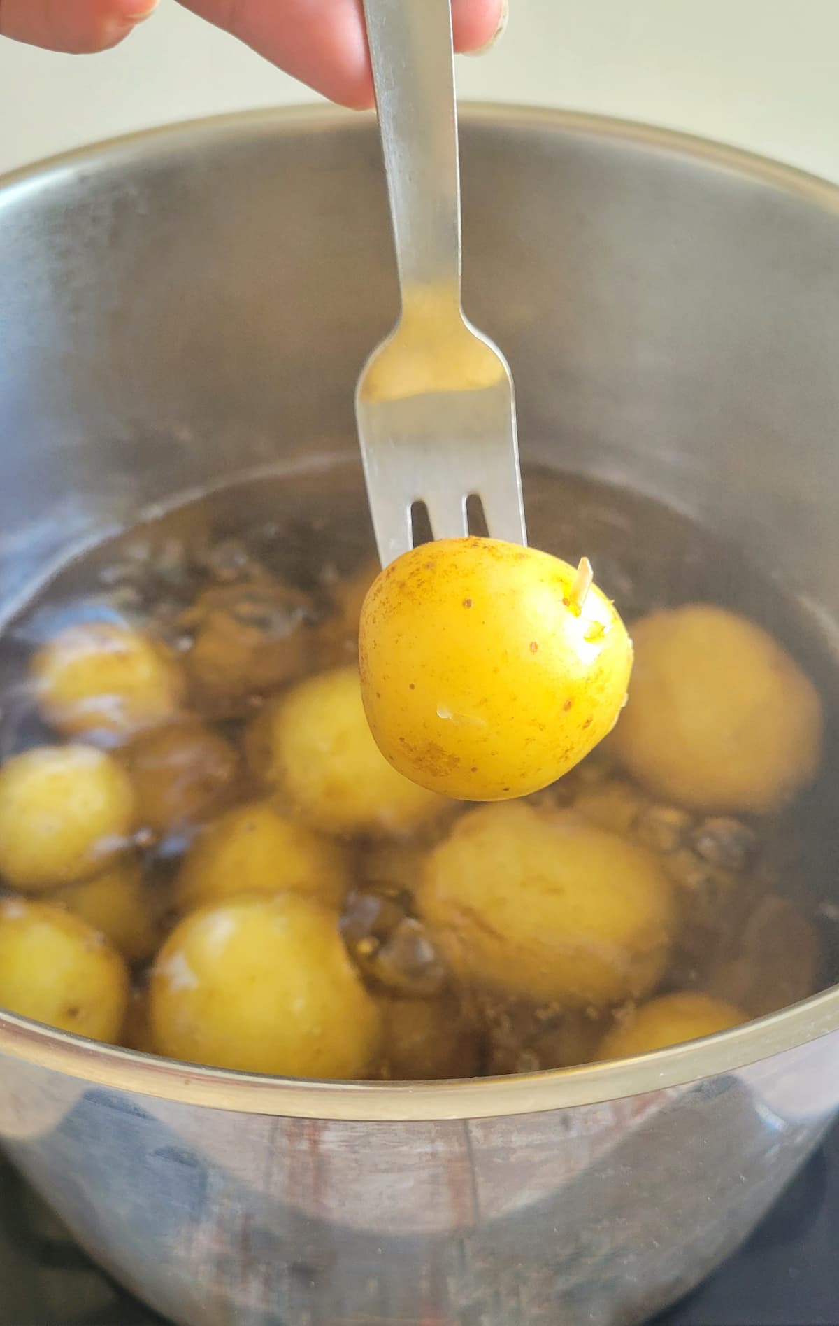 fork piercing a baby potato over a pot of the rest of them in boiling water