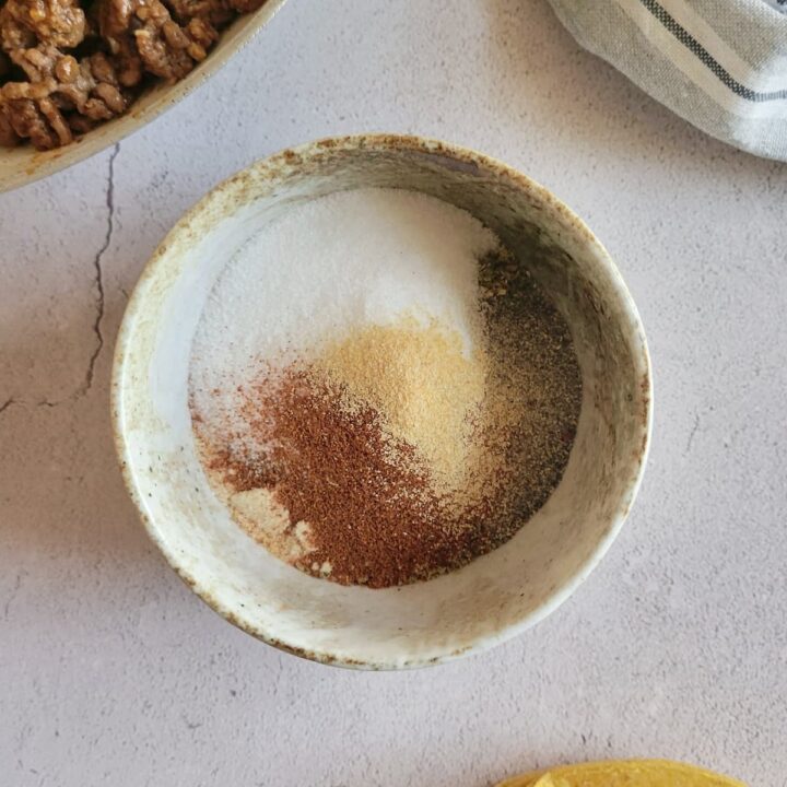 unmixed spices in a bowl next to hard taco shells and ground beef
