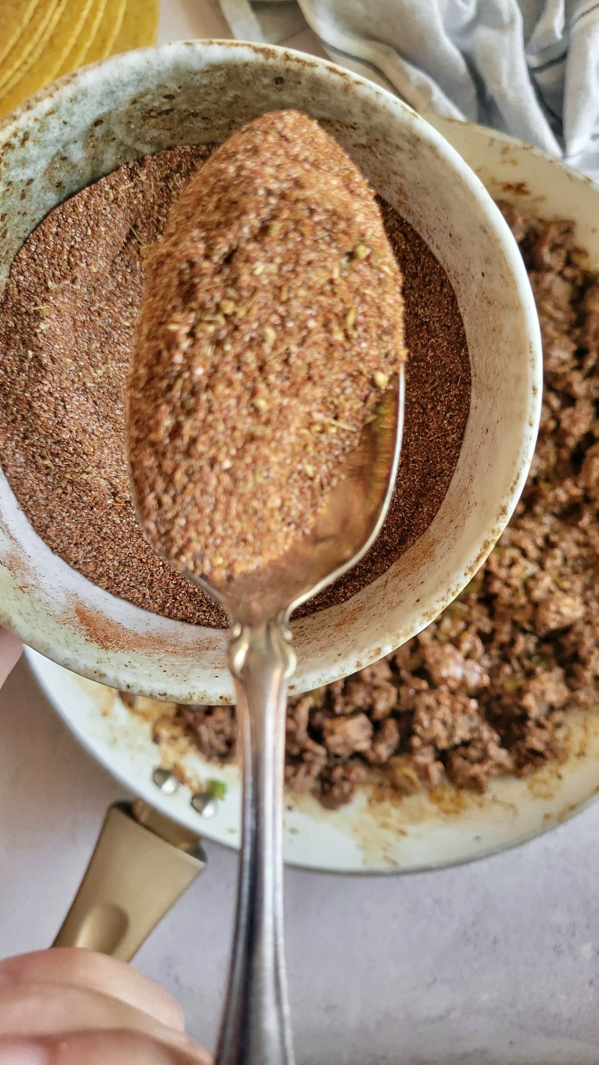 spoonful of taco mix over a bowl with the rest, skillet of ground beef in the background